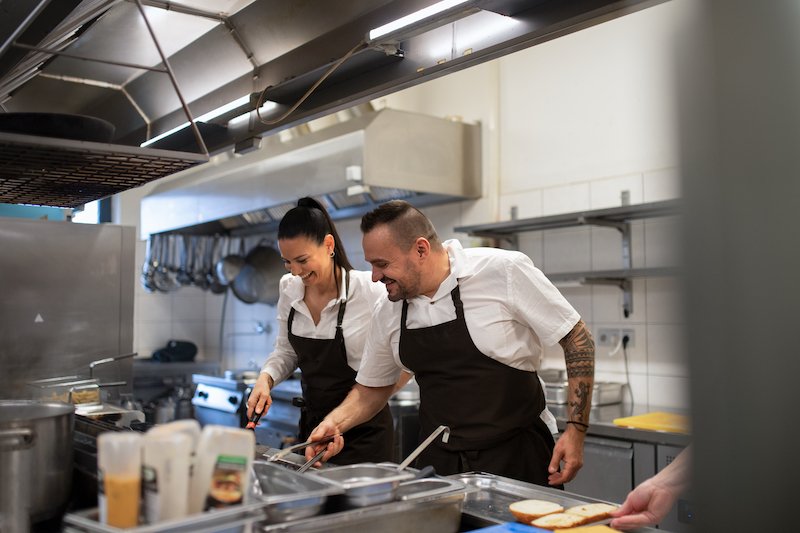 Happy chef and cook working on their dishes indoors in restaurant kitchen.